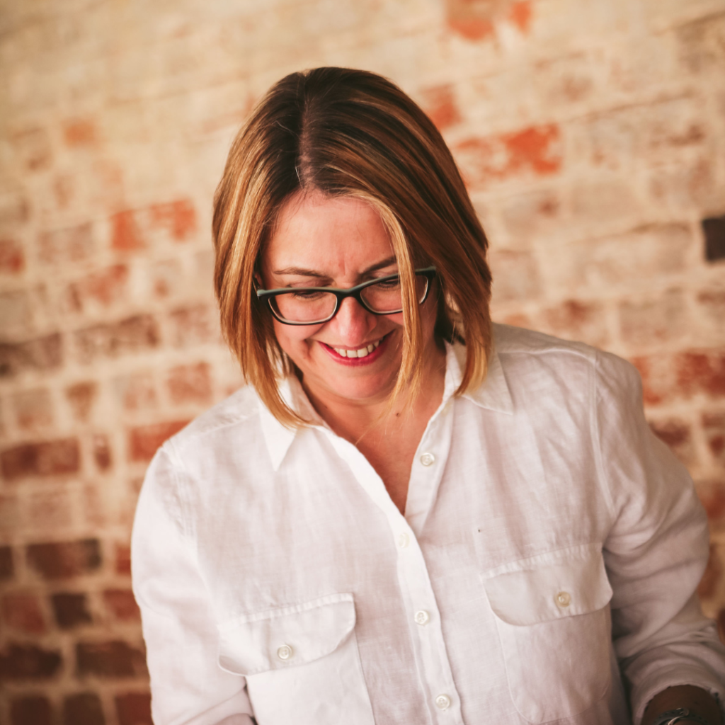 Woman wearing glasses and white shirt in front of brick wall